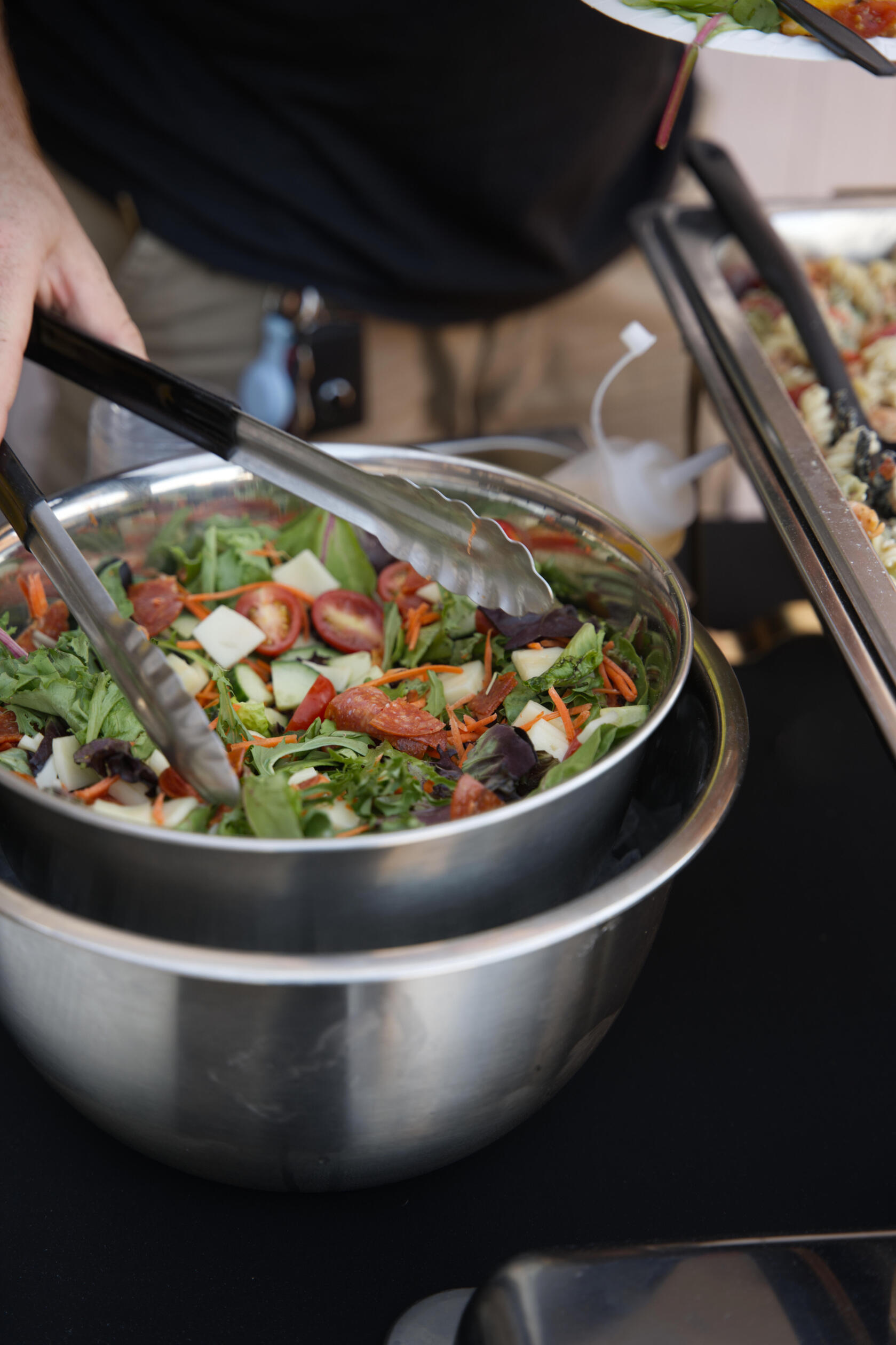 some one holding tongs, serving themselves a garden salad